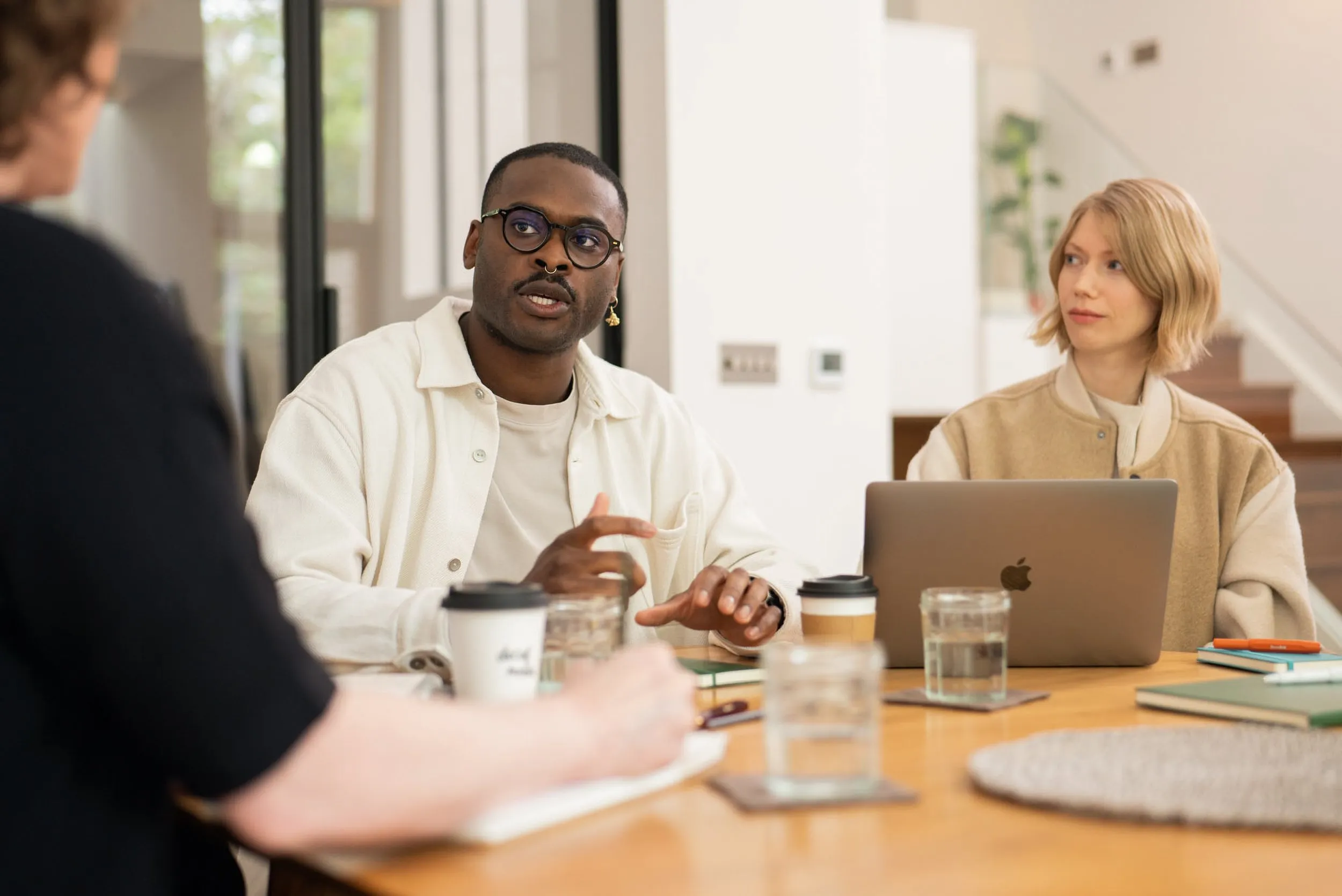 Diverse team in discussion around a table with MacBook, corporate branding photography, London