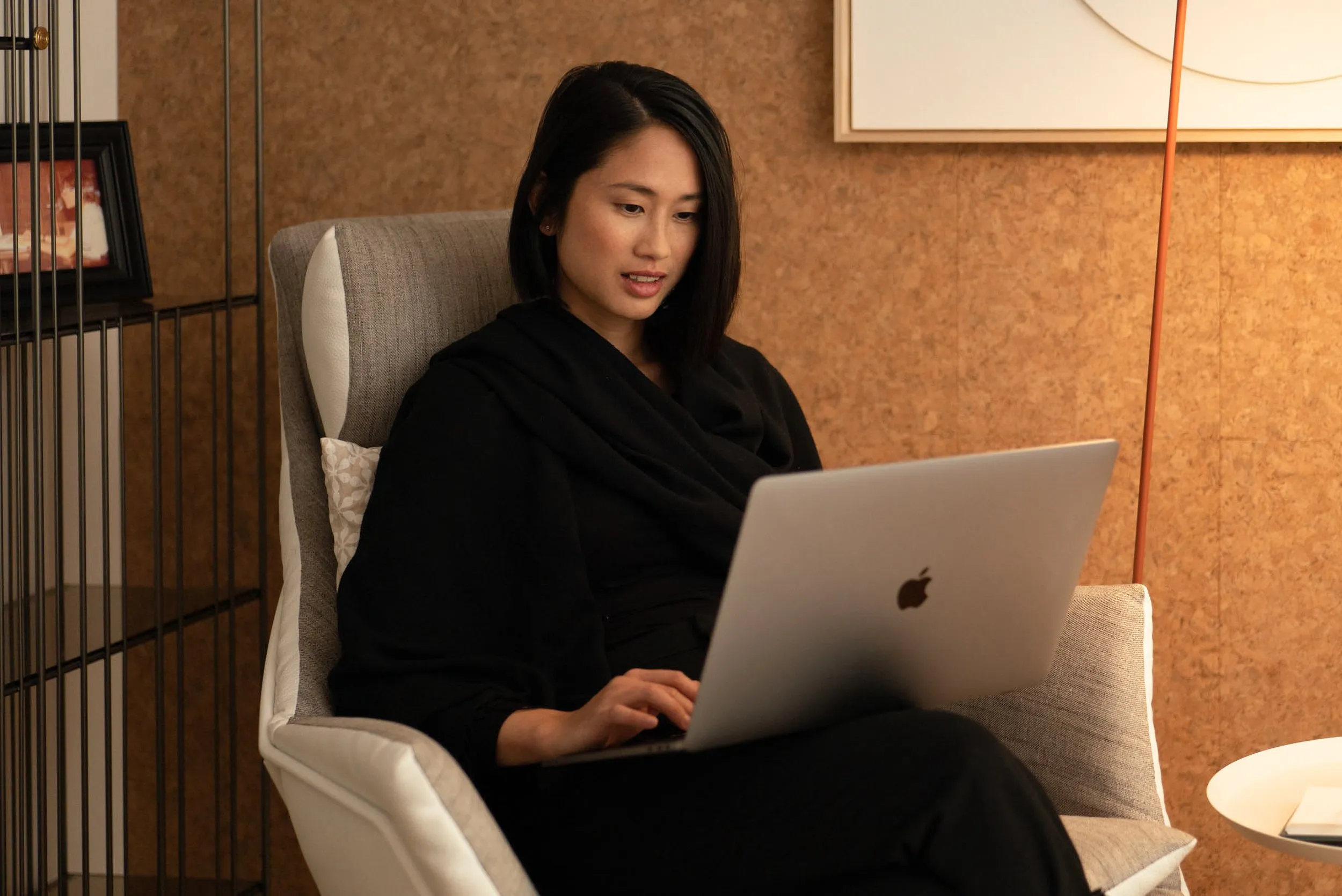 Woman working on MacBook Pro in an armchair in a modern workspace, corporate lifestyle photography