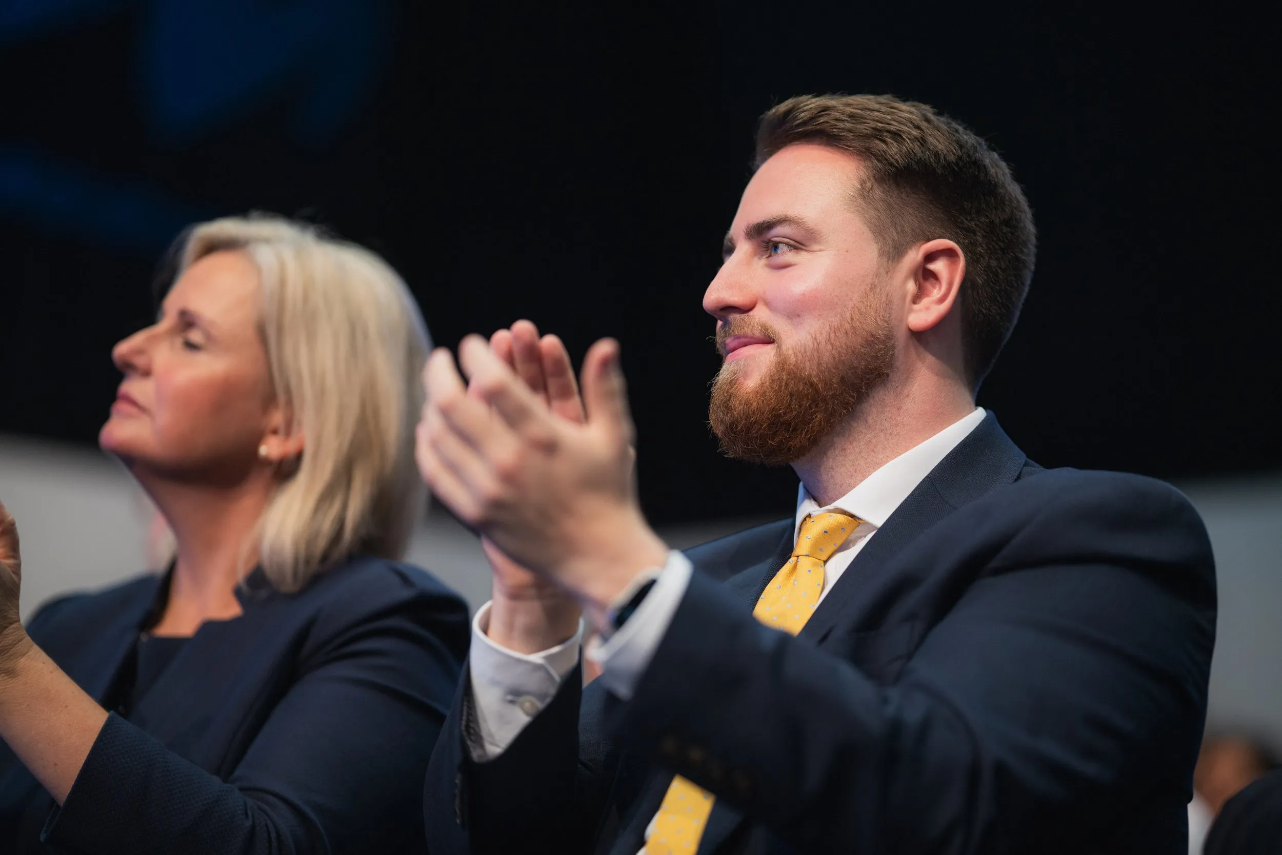 Conference delegate in navy suit applauding during a session, London conference photography