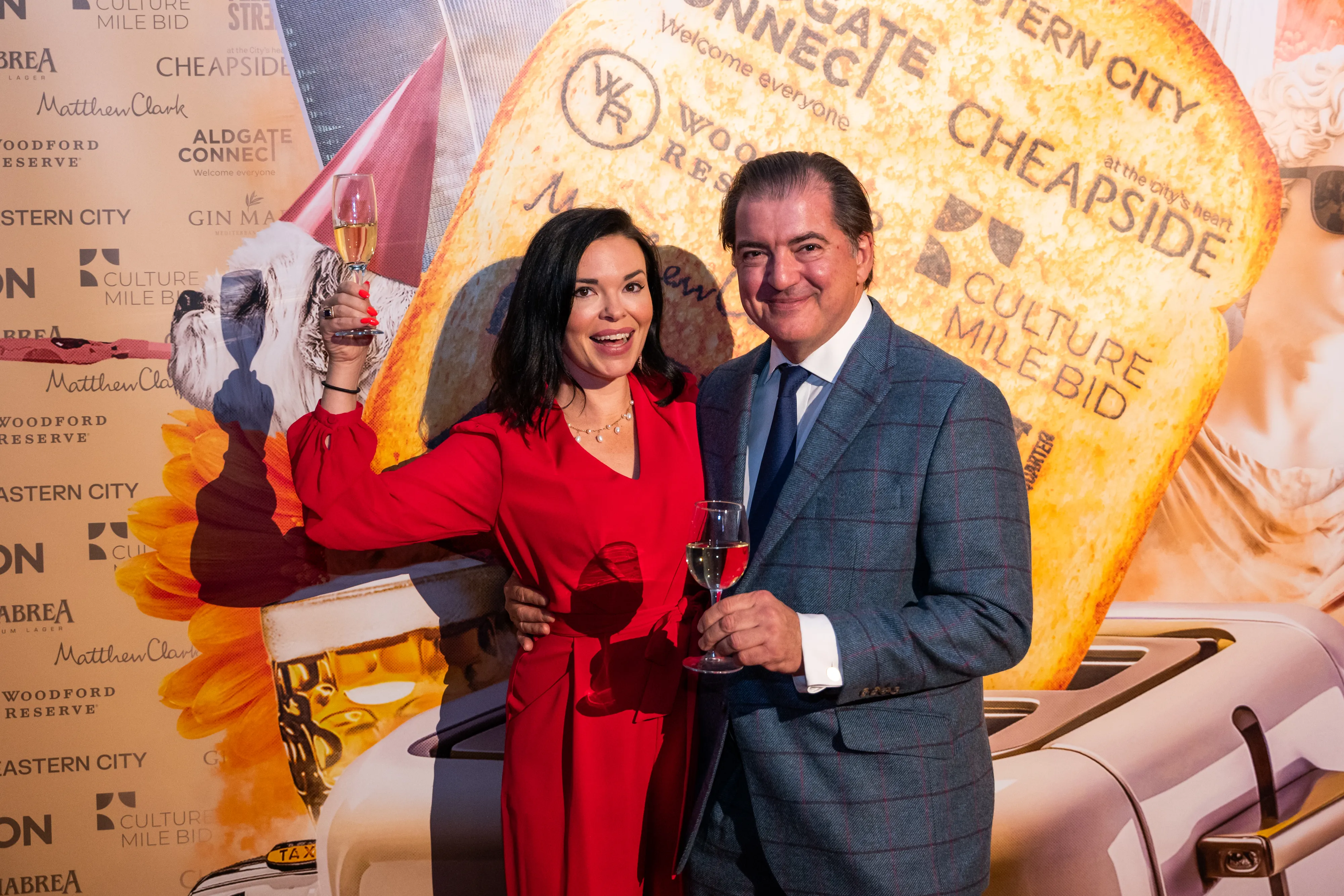 Couple toasting champagne in front of branded step-and-repeat backdrop, London event photography