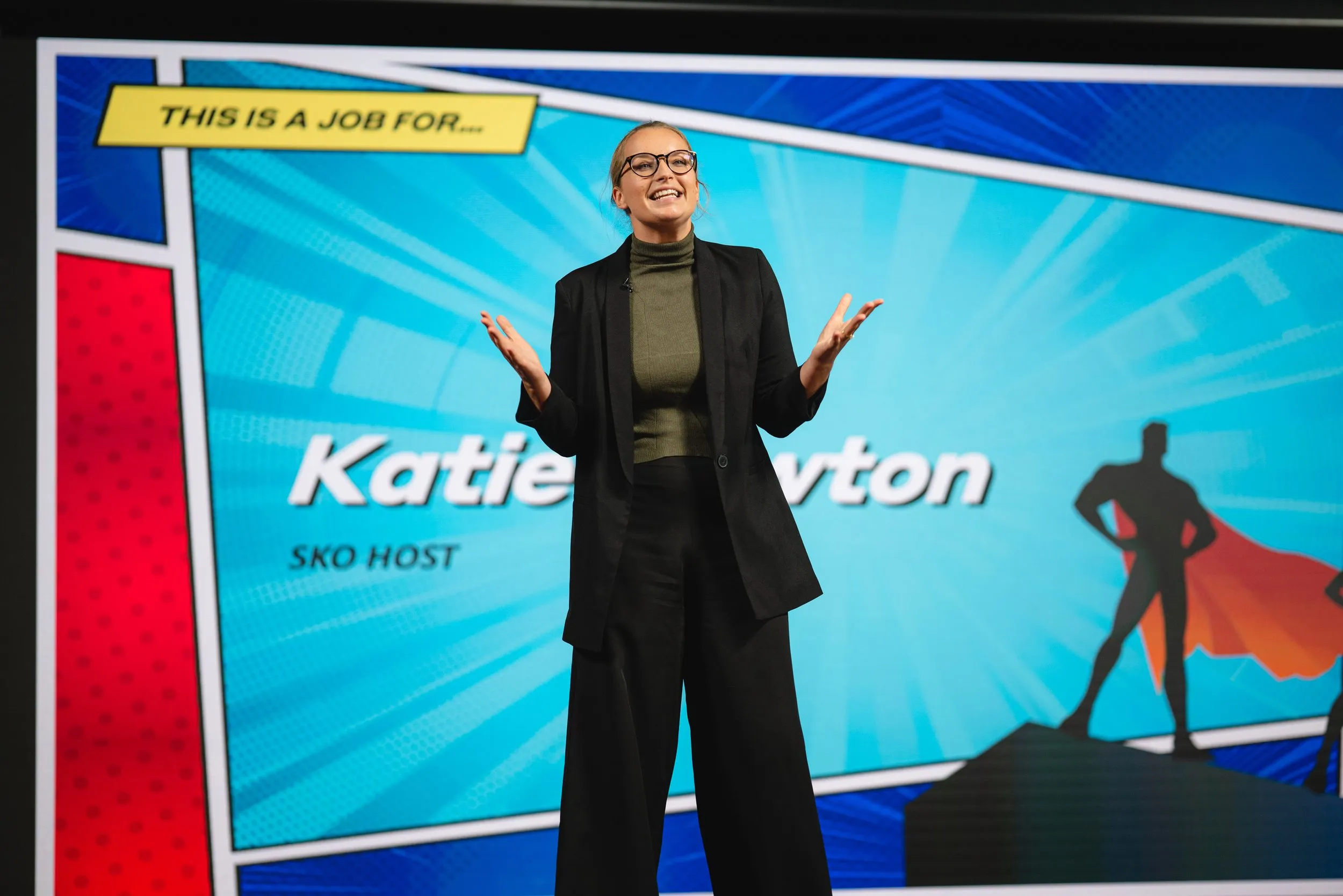 Female host presenting on stage with branded backdrop, corporate event photography London