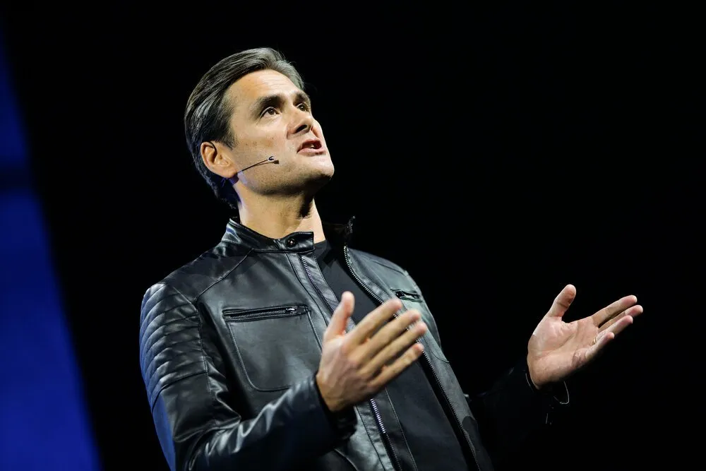 Keynote speaker on large dark stage with bright projected screen behind, London conference photography