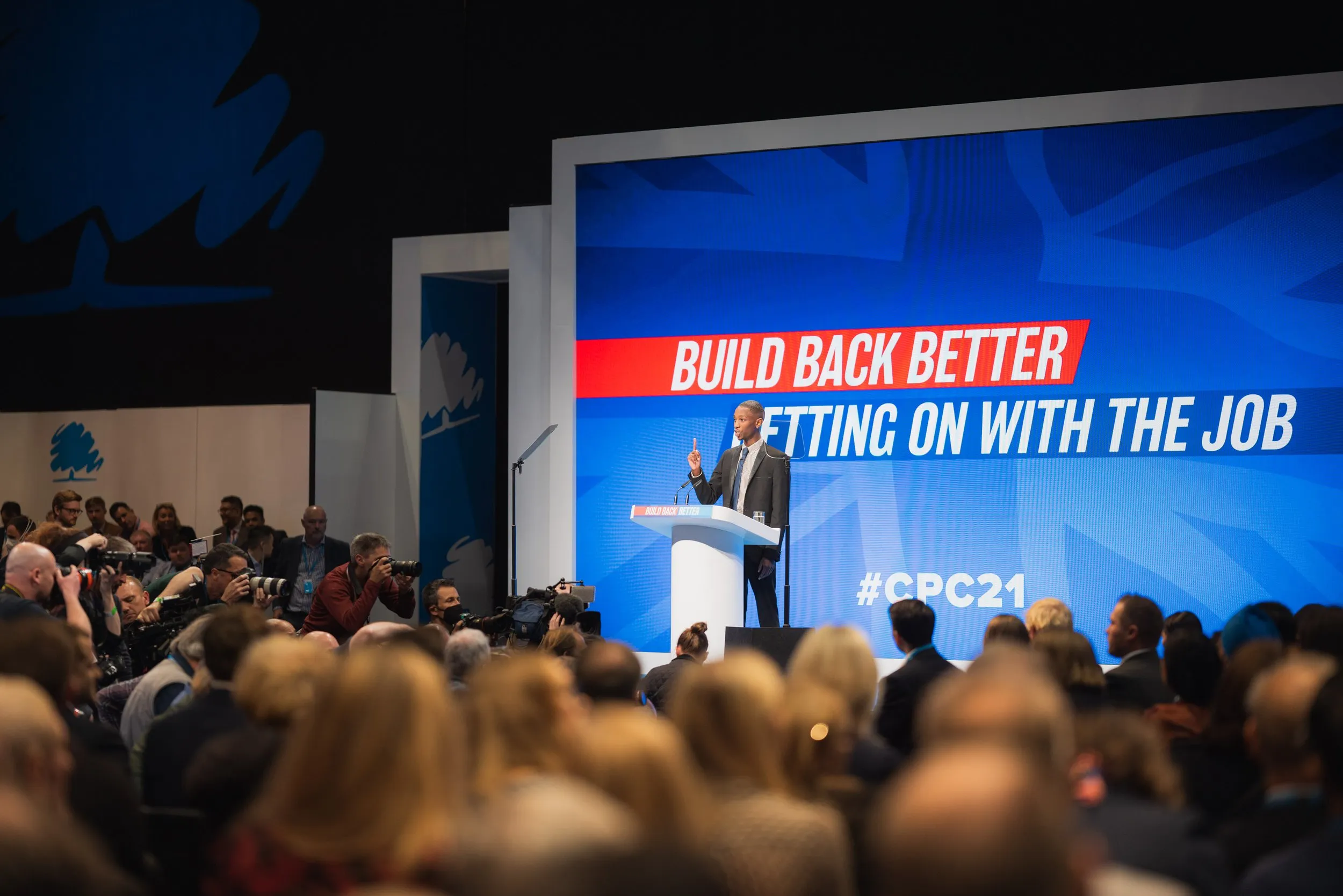 Conference photography of keynote speaker on stage at large-screen political conference, London
