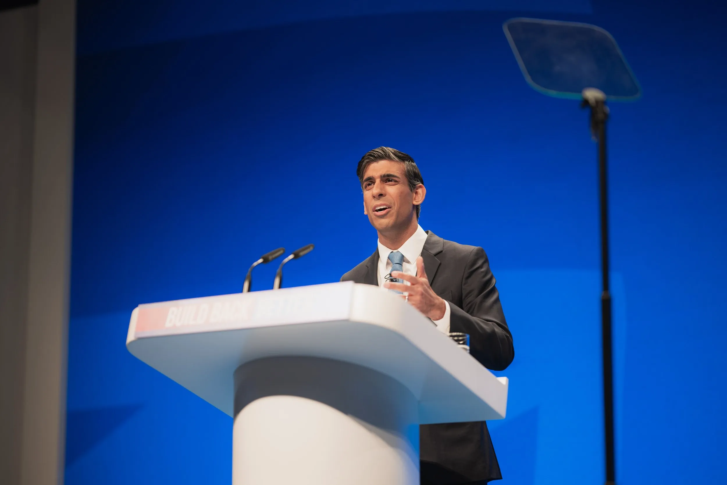 Political conference speaker at lectern with blue branded backdrop, London conference photography
