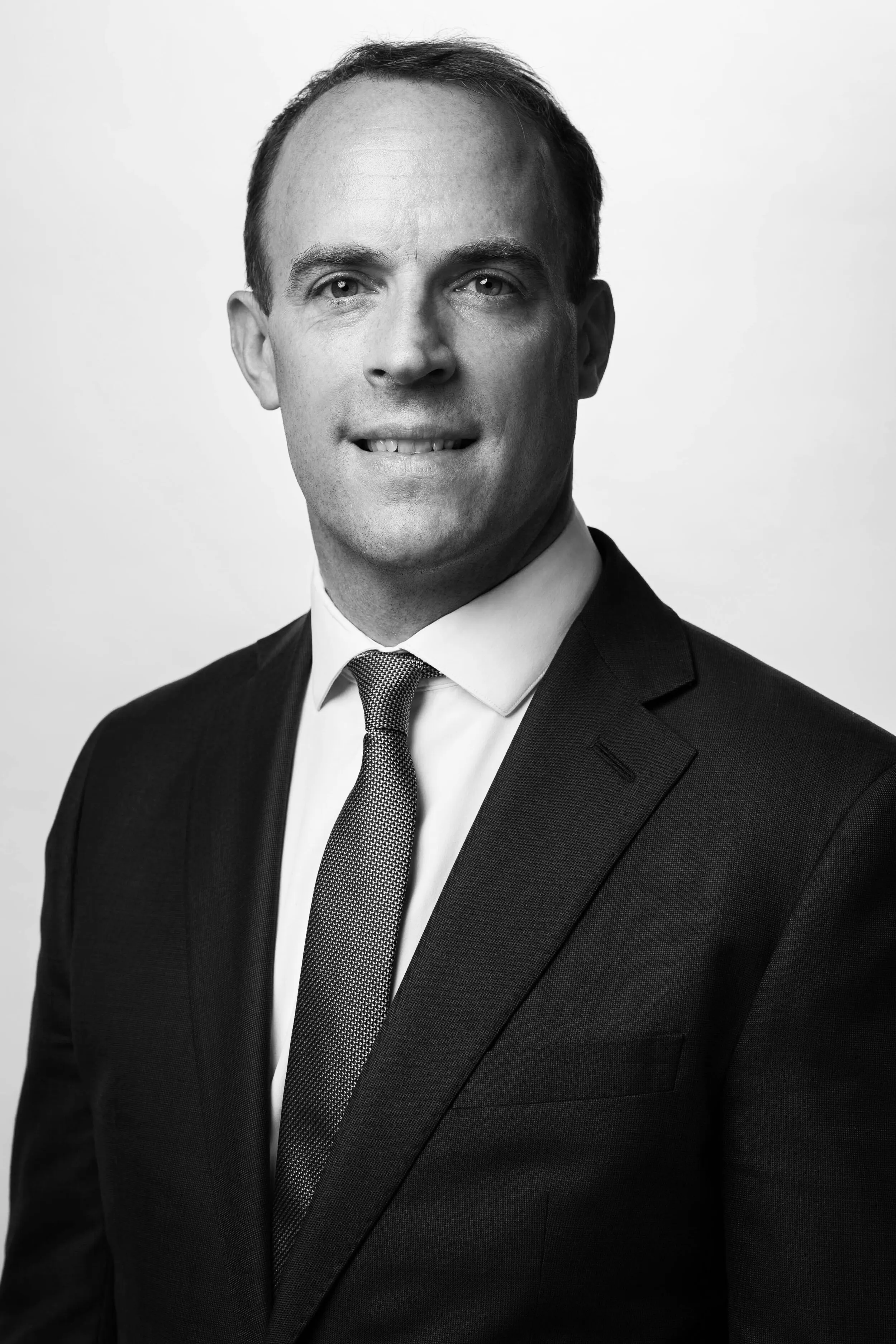 Black and white formal headshot of man in black suit and tie, London