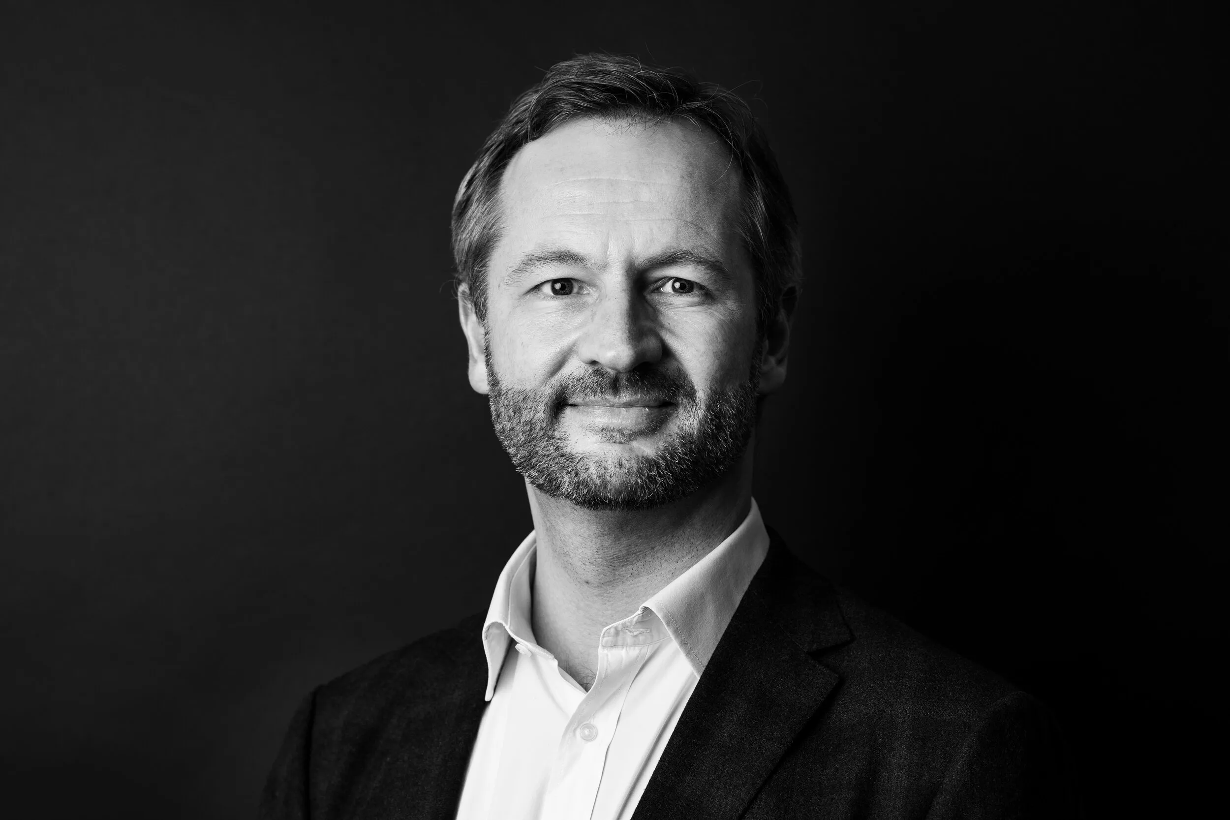 Black and white corporate headshot of man with beard in dark blazer, London