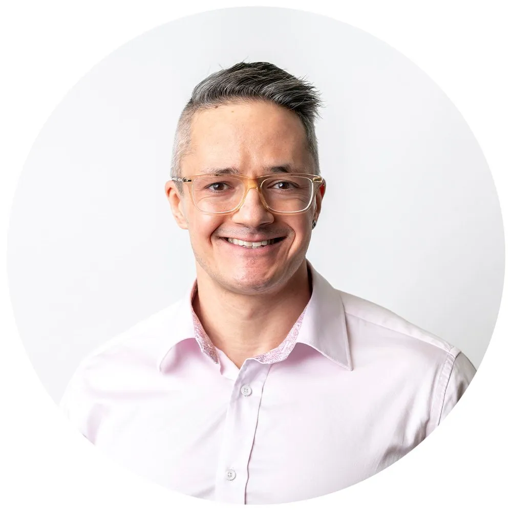 Smiling corporate headshot of man in glasses and pink shirt, London