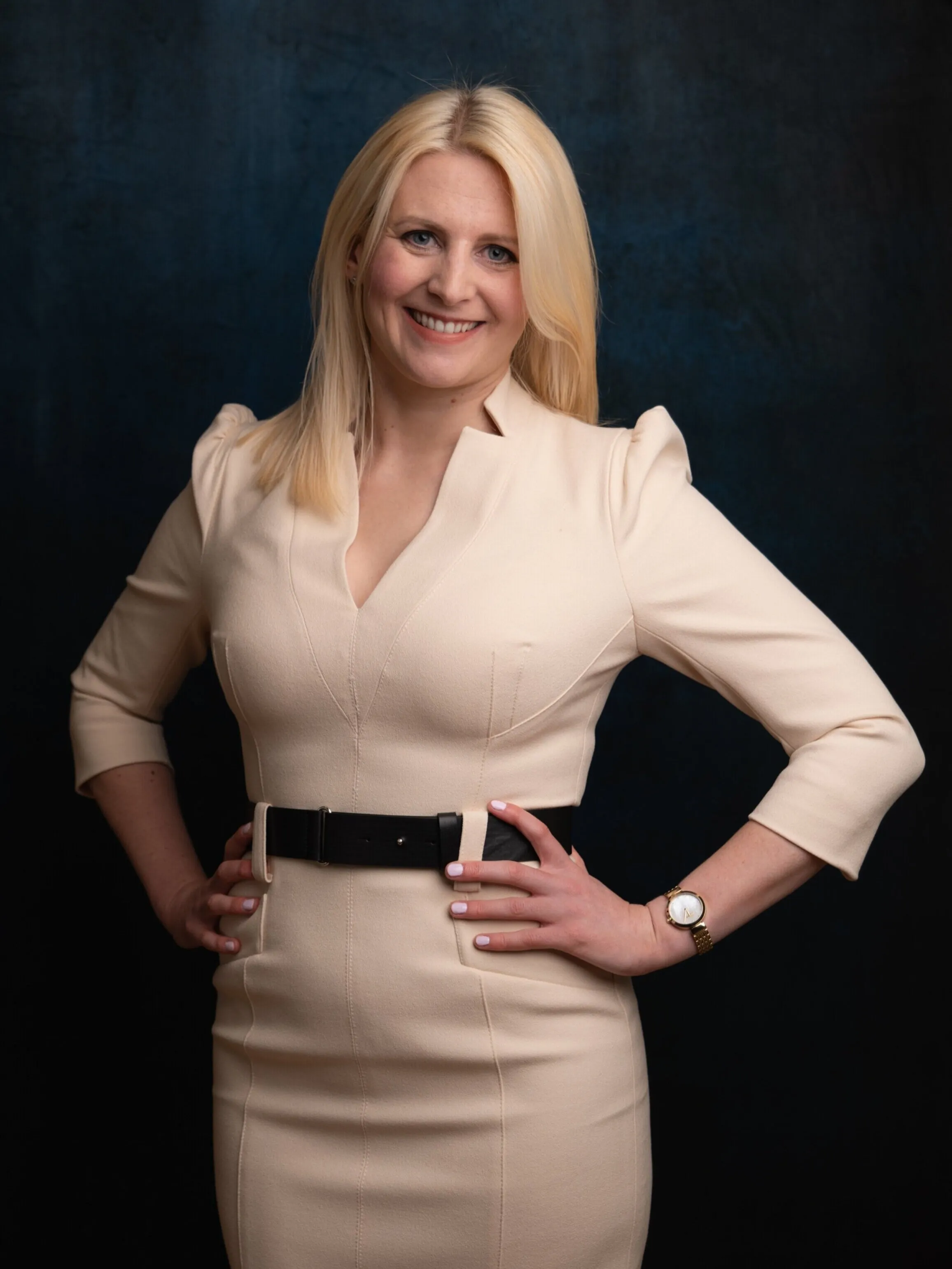 Professional headshot of blonde woman in cream dress, dark background, London
