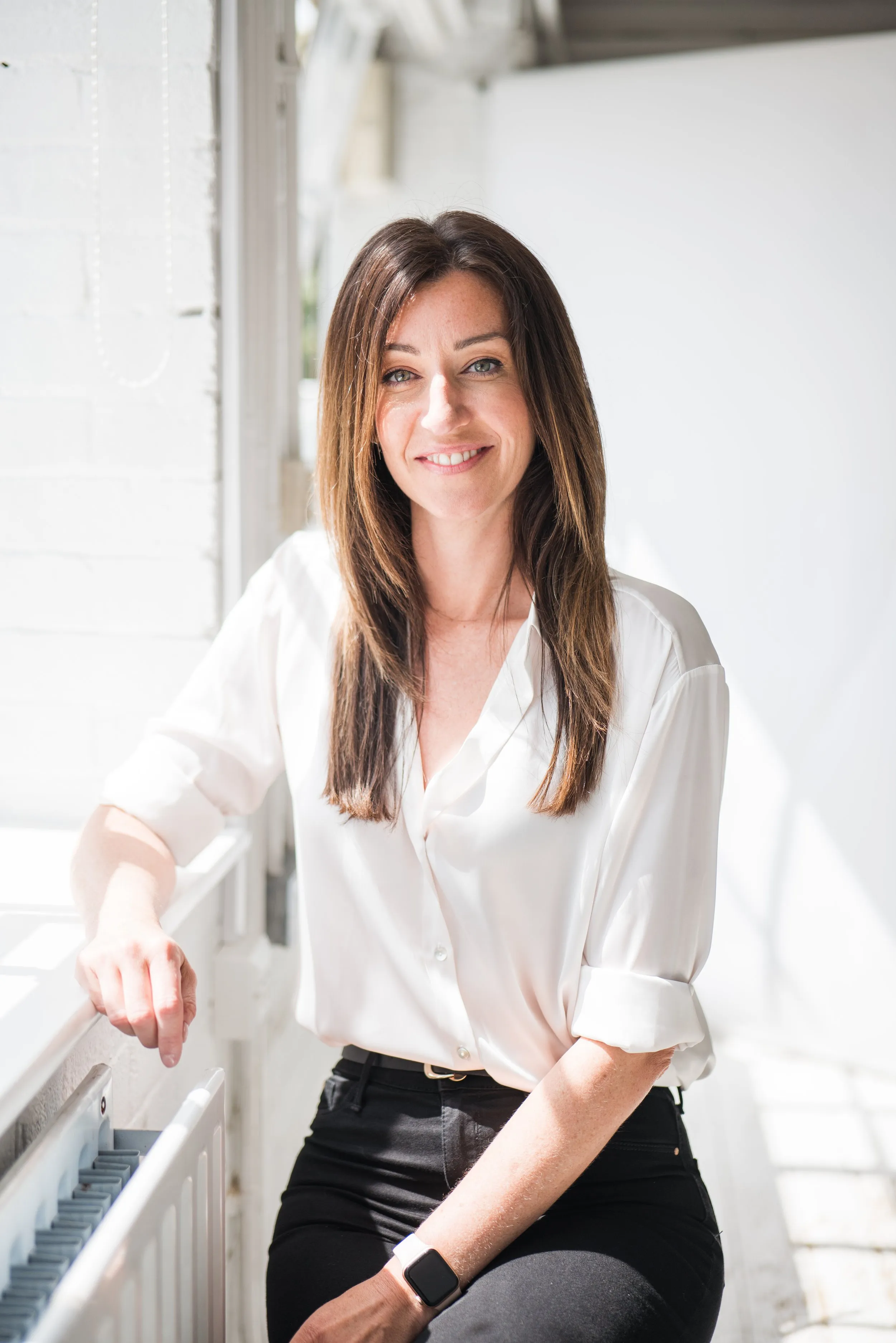 Professional headshot of brunette woman in white blouse on staircase, natural light, London