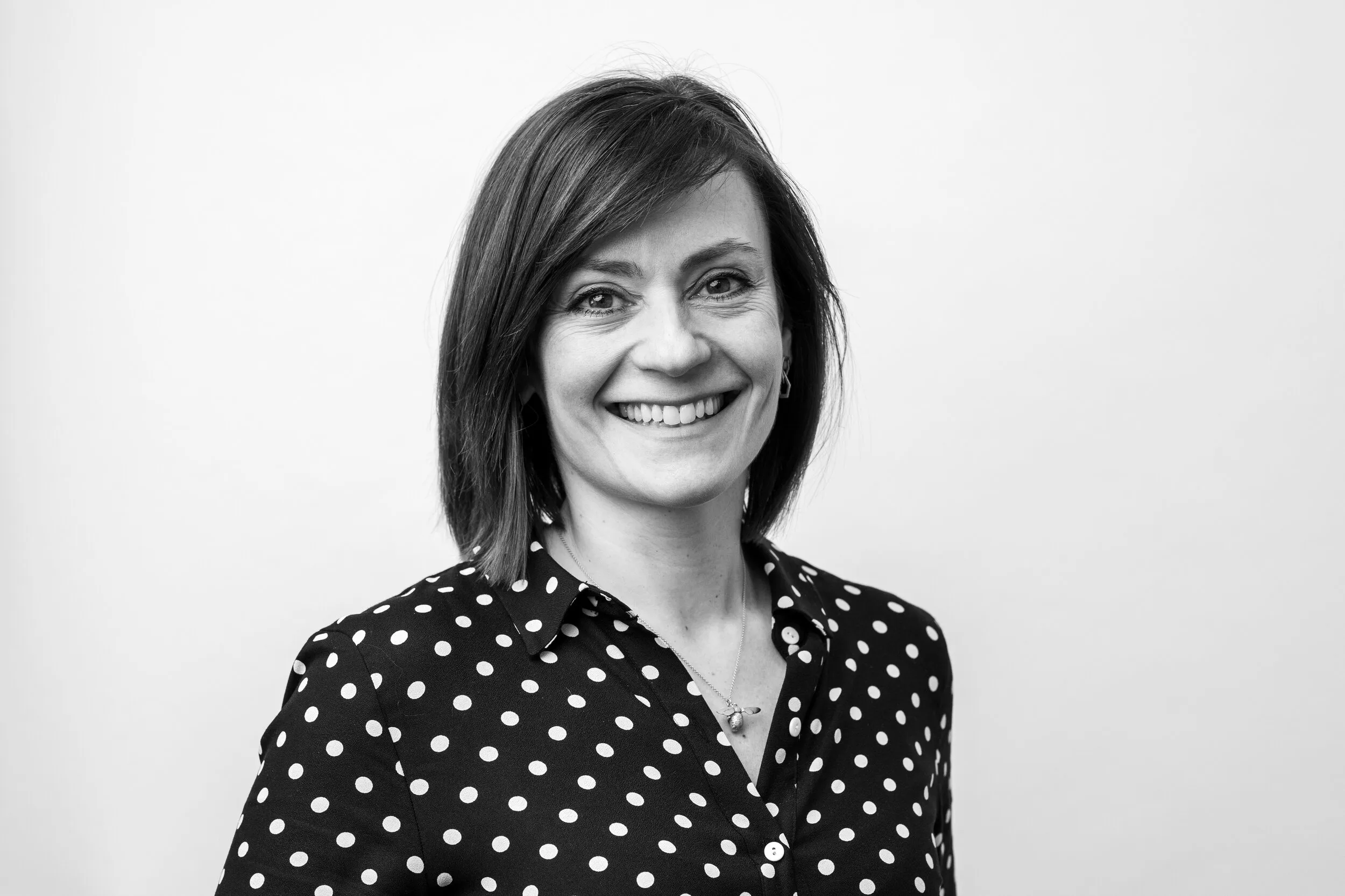 Black and white professional headshot of woman with dark hair in polka dot blouse, London