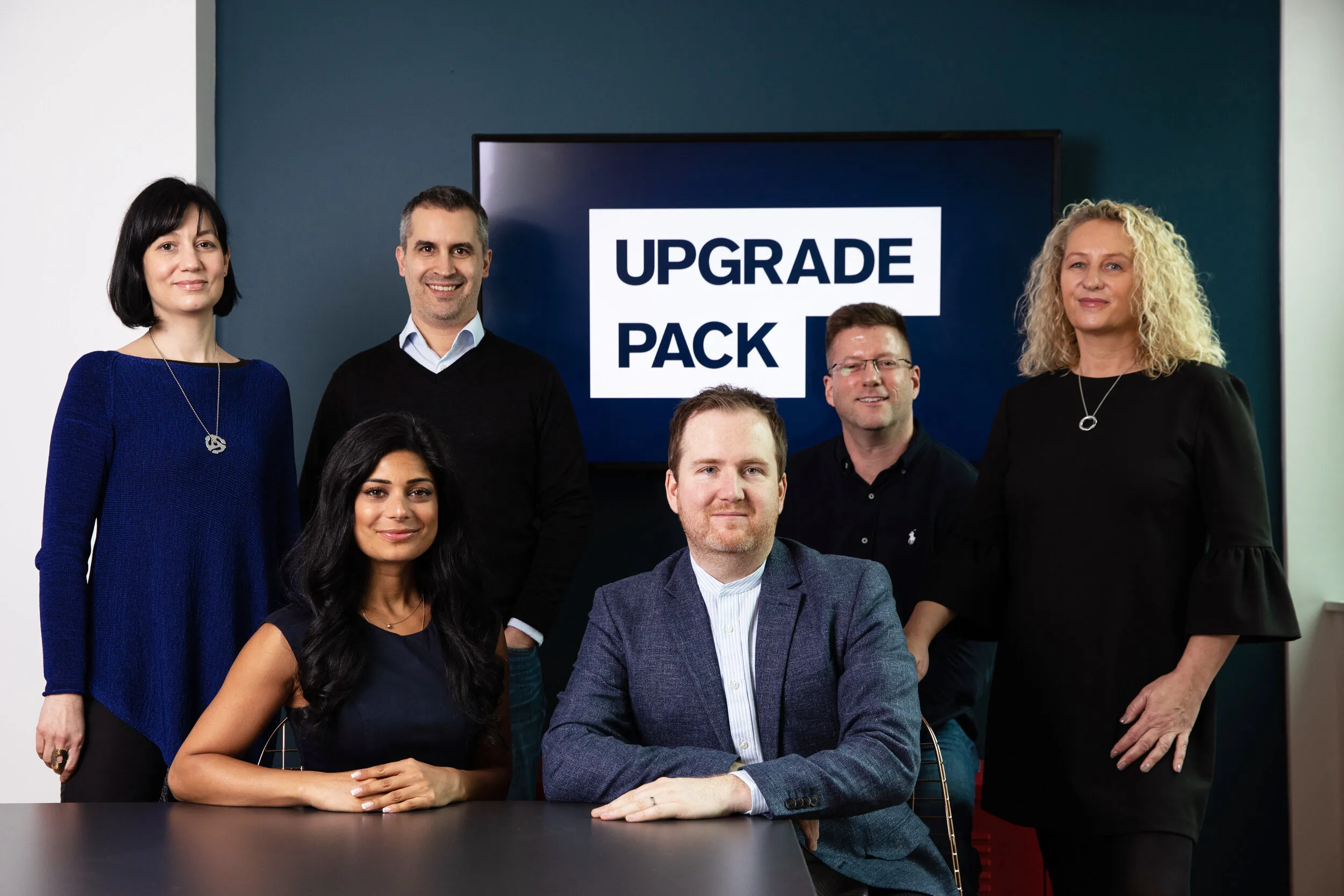 Six-person executive team photographed in a London boardroom with company branding